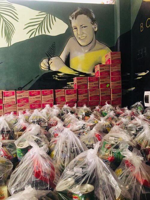 A painting of a boy on a surfboard is behind a bunch of bags of food