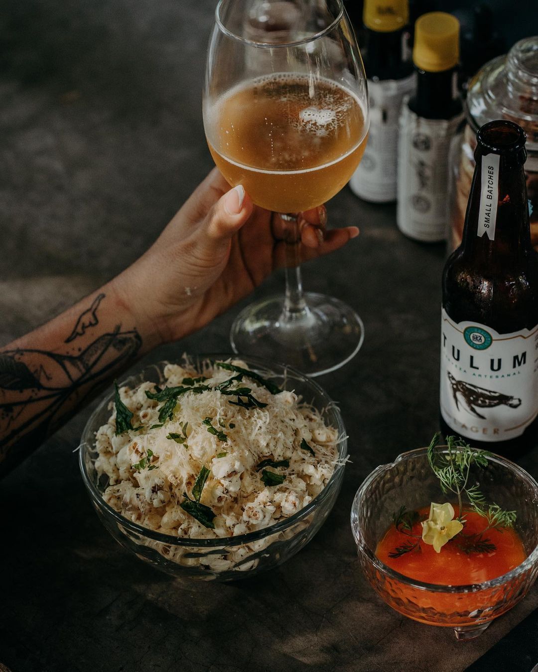 A person is holding a glass of beer next to a bowl of food.