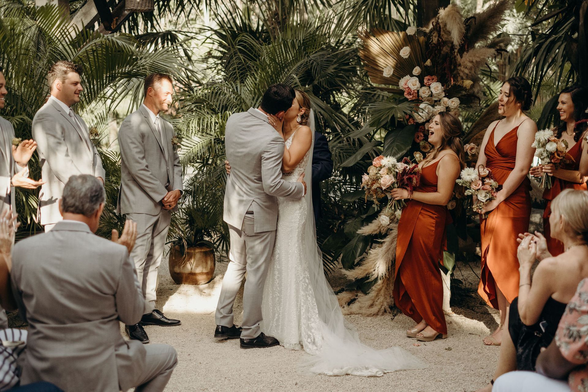 A bride and groom are kissing at WILD Tulum during their wedding ceremony while their wedding party watches.