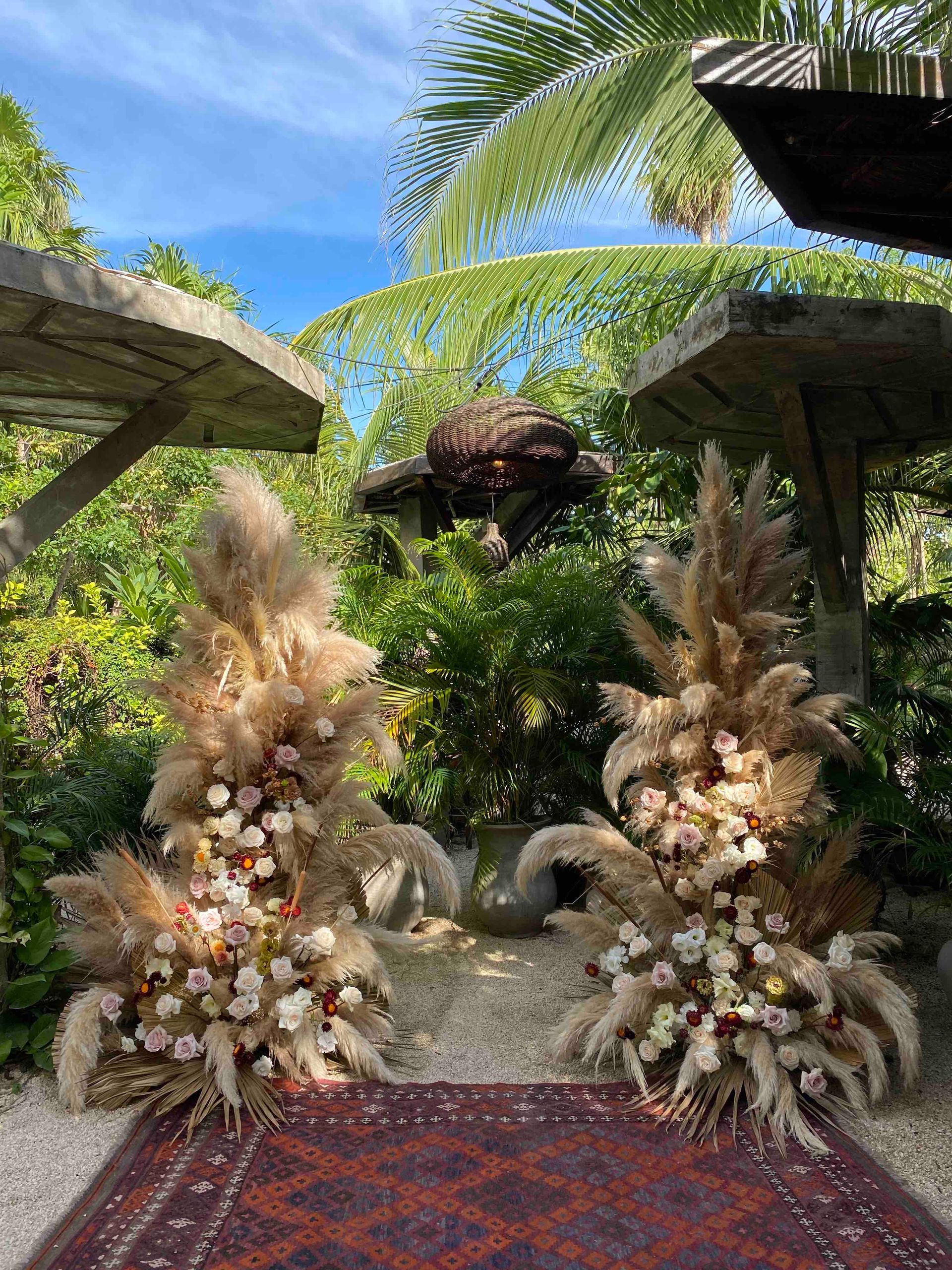 A boho chic wedding alter for the ceremony at WILD Tulum. There is a rug in the foreground and flowers in the background
