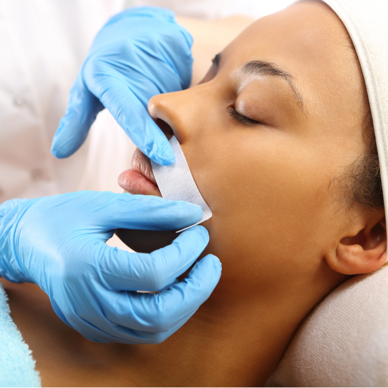 A woman wearing blue gloves is getting her lips waxed