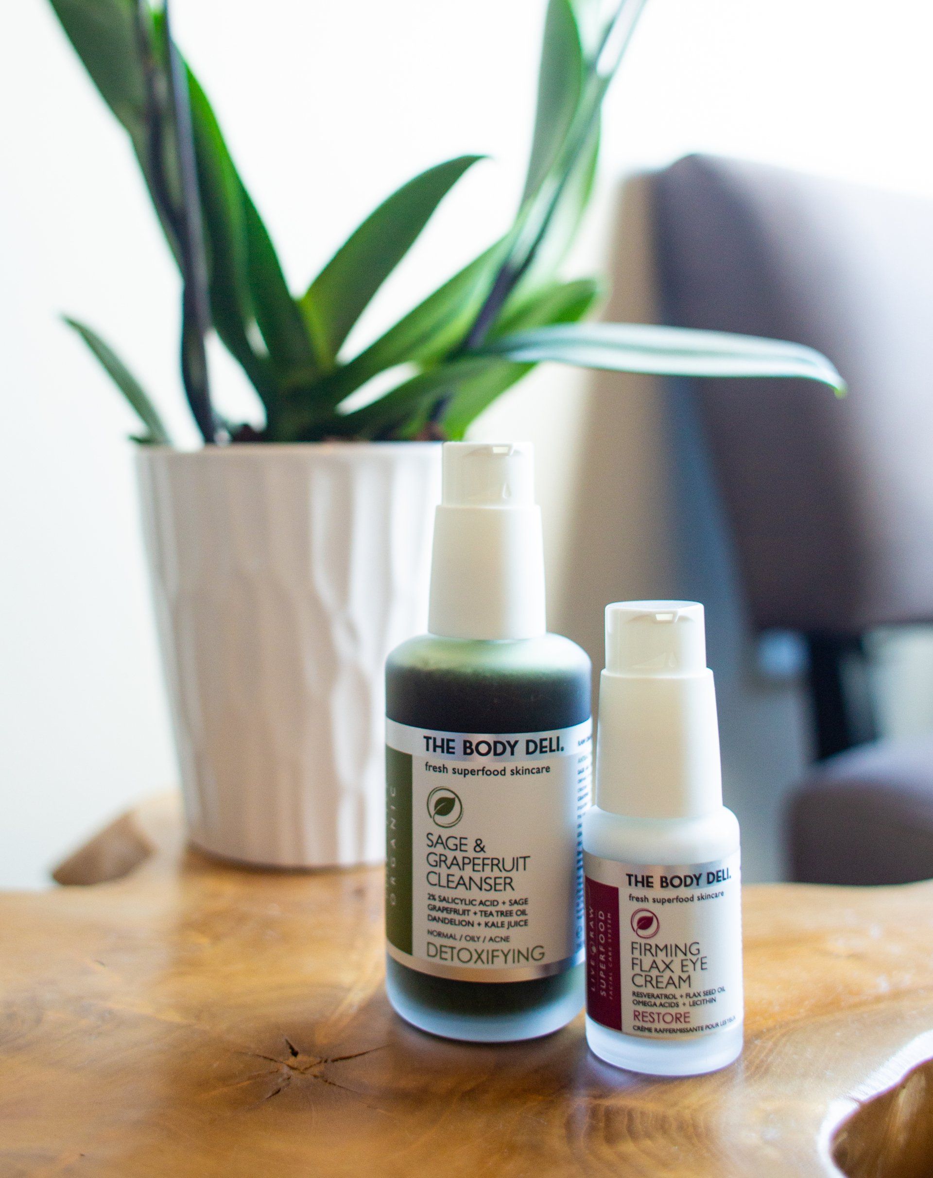 Two bottles of lotion are sitting on a wooden table next to a potted plant.
