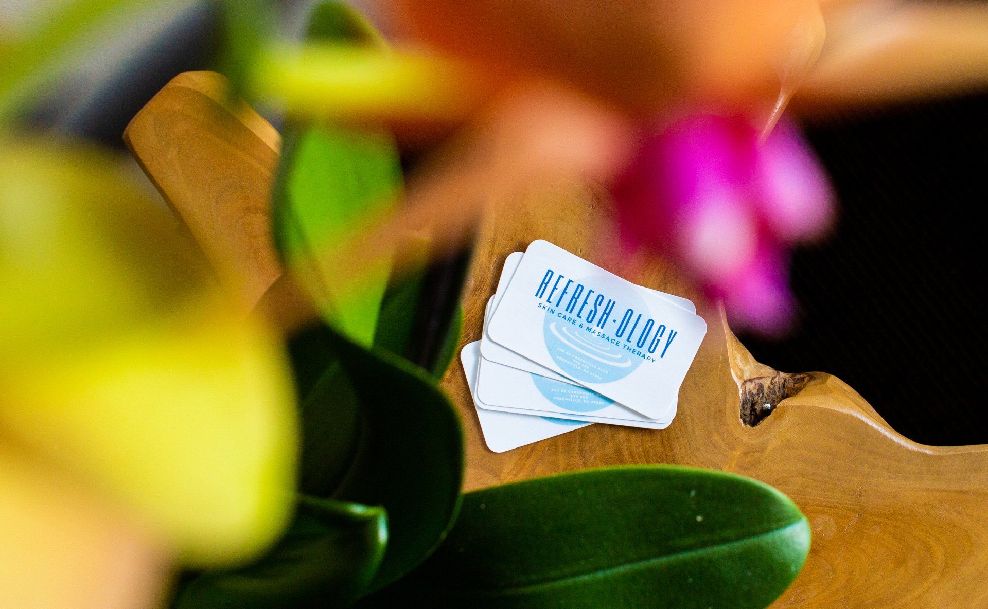 Two business cards are sitting on a wooden table next to a flower.