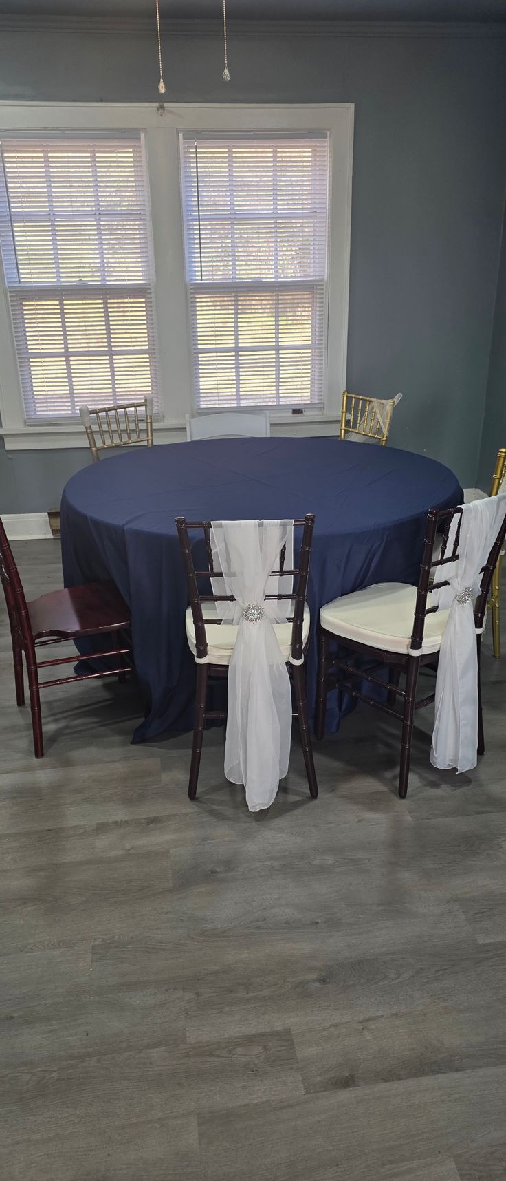 A round table covered with a navy tablecloth is surrounded by chairs, some with white fabric tied to the backs.