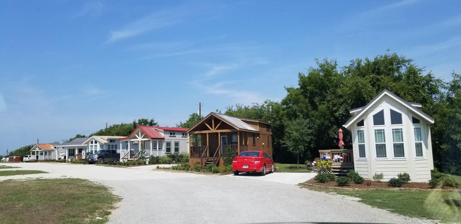 Tiny colorful houses on a gravel road under a bright blue sky. Red car parked in front of one.