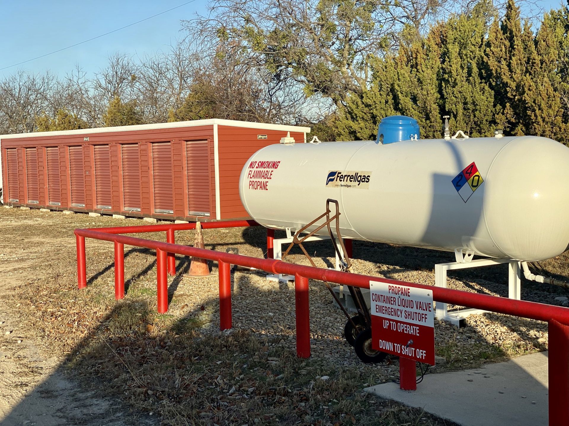 Propane tank with red safety rail and shed in a grassy field.