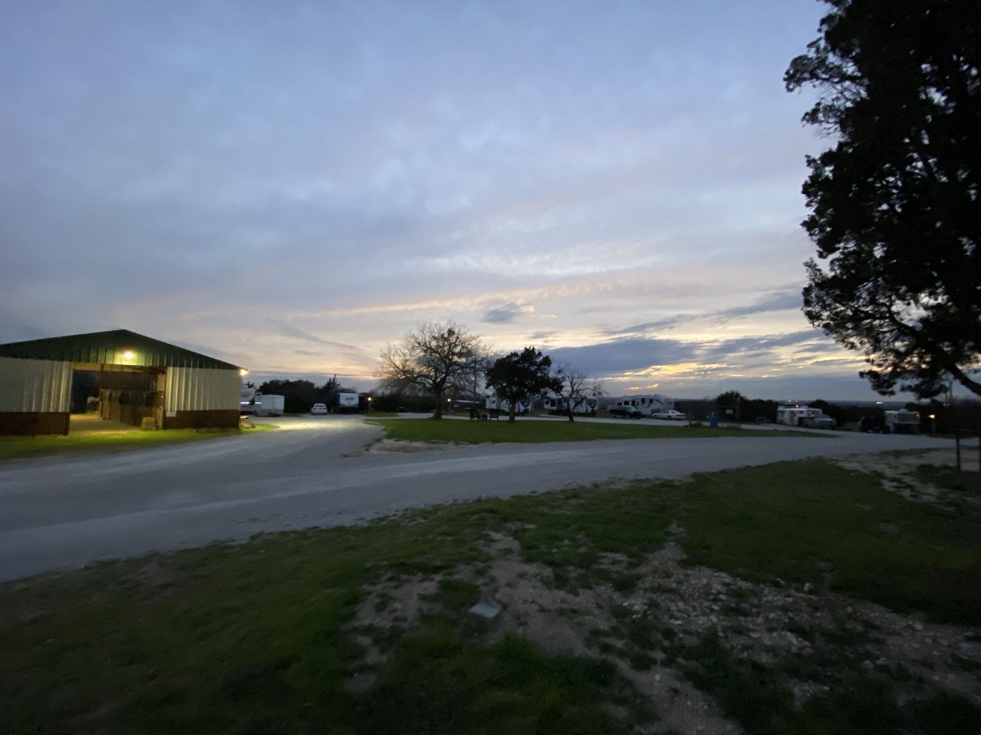 A dusk view of a campground, with a building to the left and RVs in the distance, under a cloudy sky.