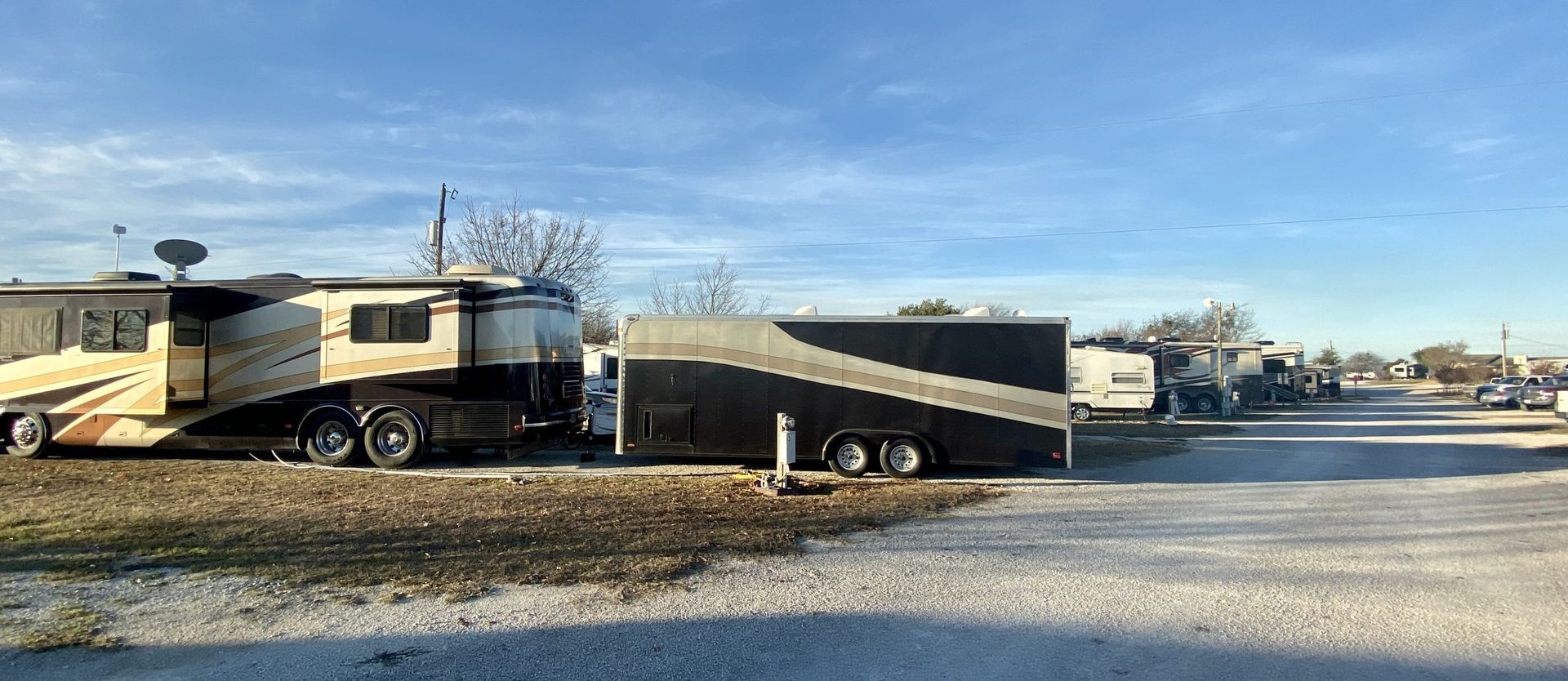 RVs and trailers parked along a gravel road under a bright blue sky.