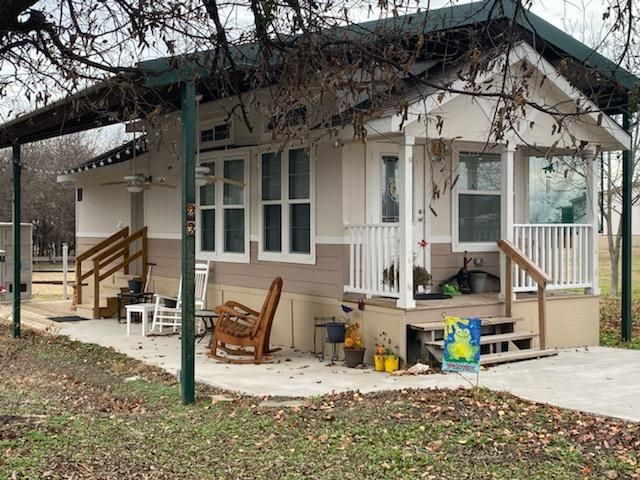 Tan and white house with porch and awning. Green posts. Rocking chair. Concrete patio.