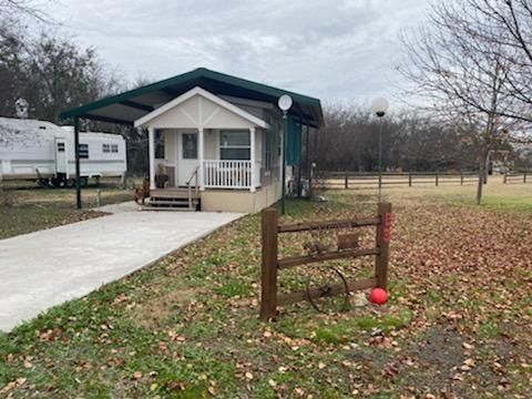 Small white cottage with covered porch and RV in background, on a grassy lot.