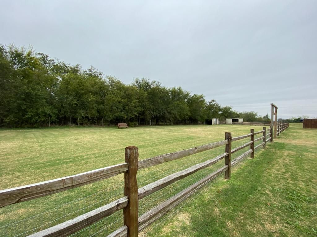 Wooden fence in grassy field with trees under a cloudy sky.