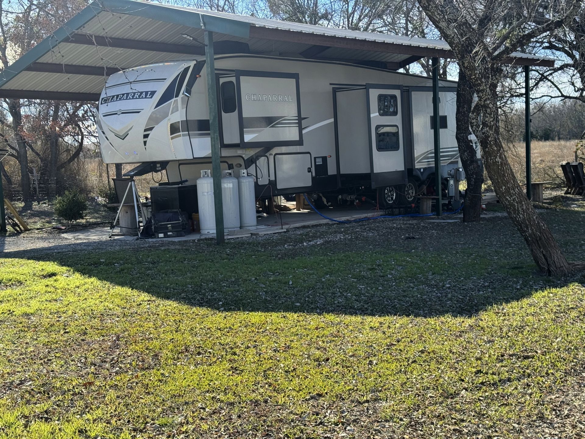 RV parked under a metal carport in a grassy outdoor setting.