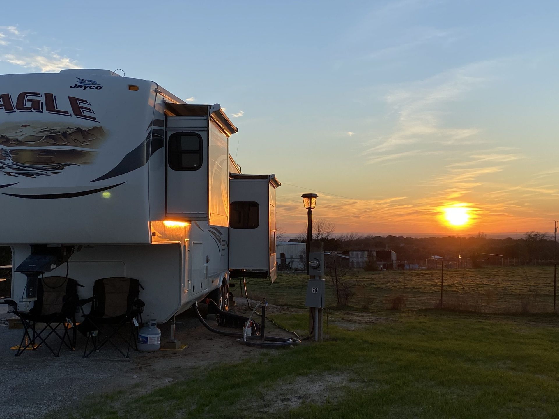 RV parked on grass at sunset with a bright orange sky.