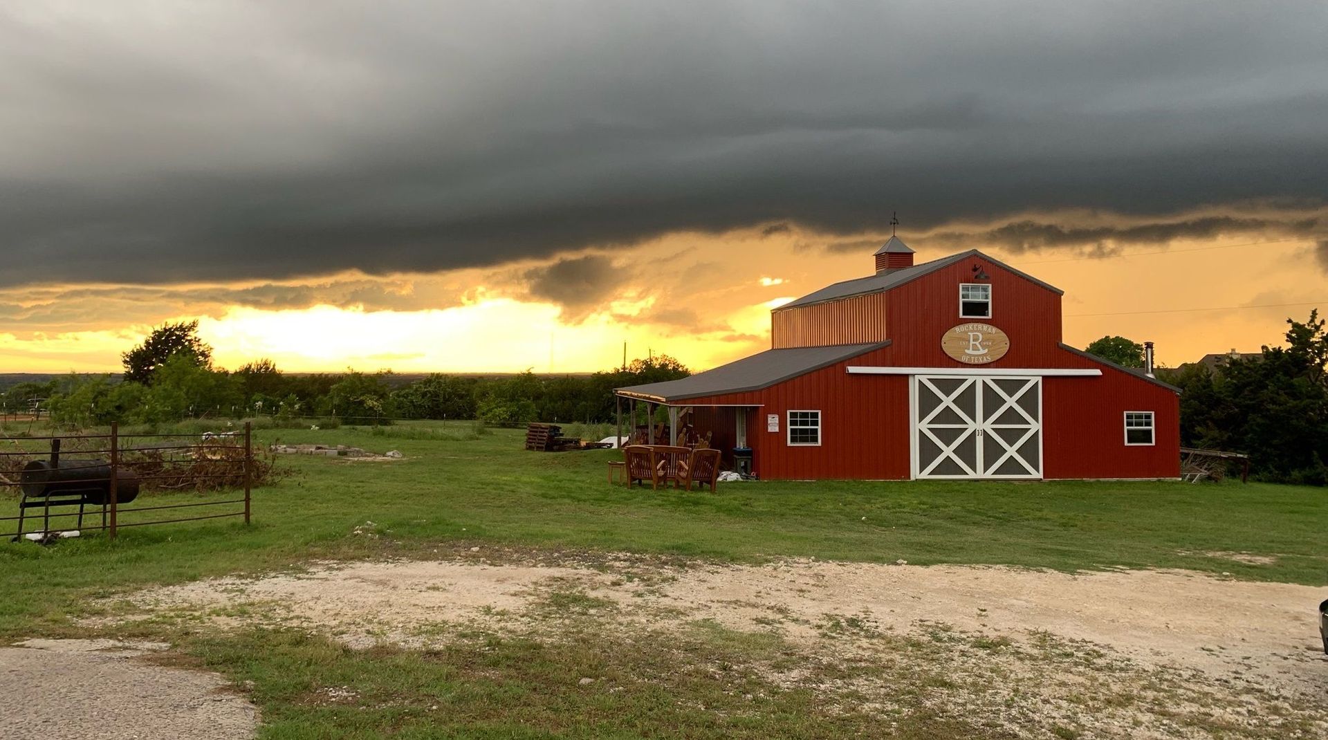 Red barn with white cross-braced doors under a stormy orange sky.