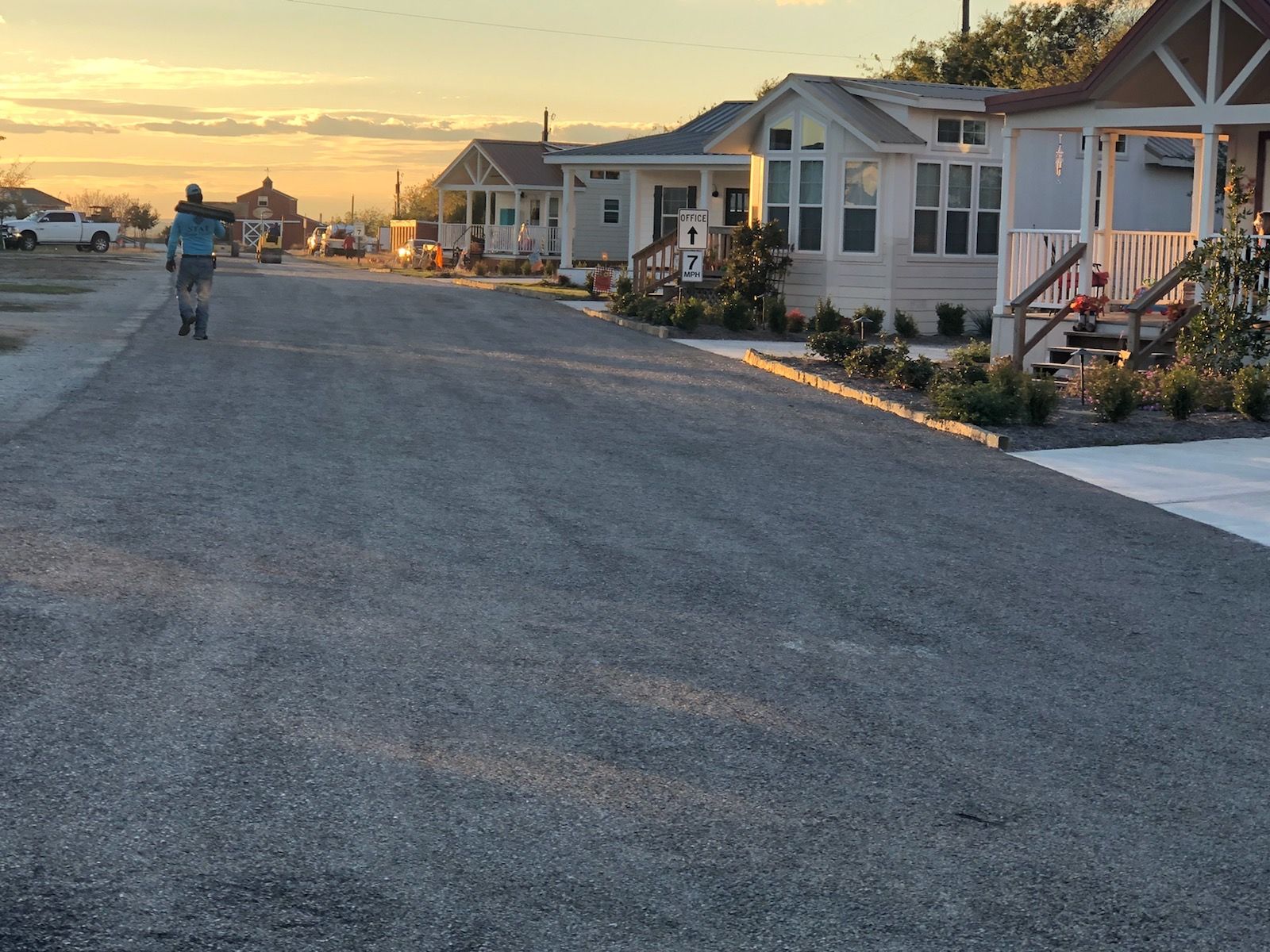 Person riding a scooter down a gravel road lined with small houses at dusk.