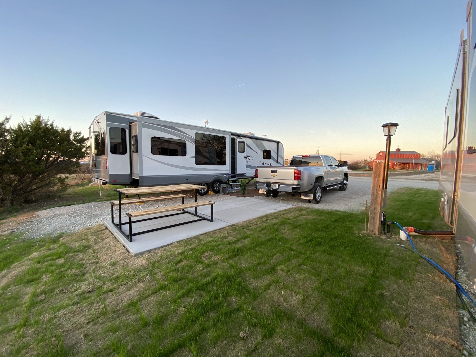 RV and pickup truck parked at campsite next to a picnic table, with grass and gravel.
