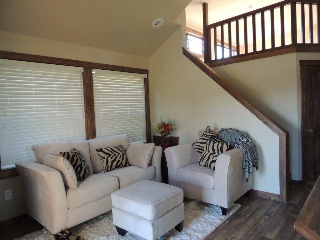 Living room with sofa, armchair, ottoman, rug, stairs to a second level, and window blinds.