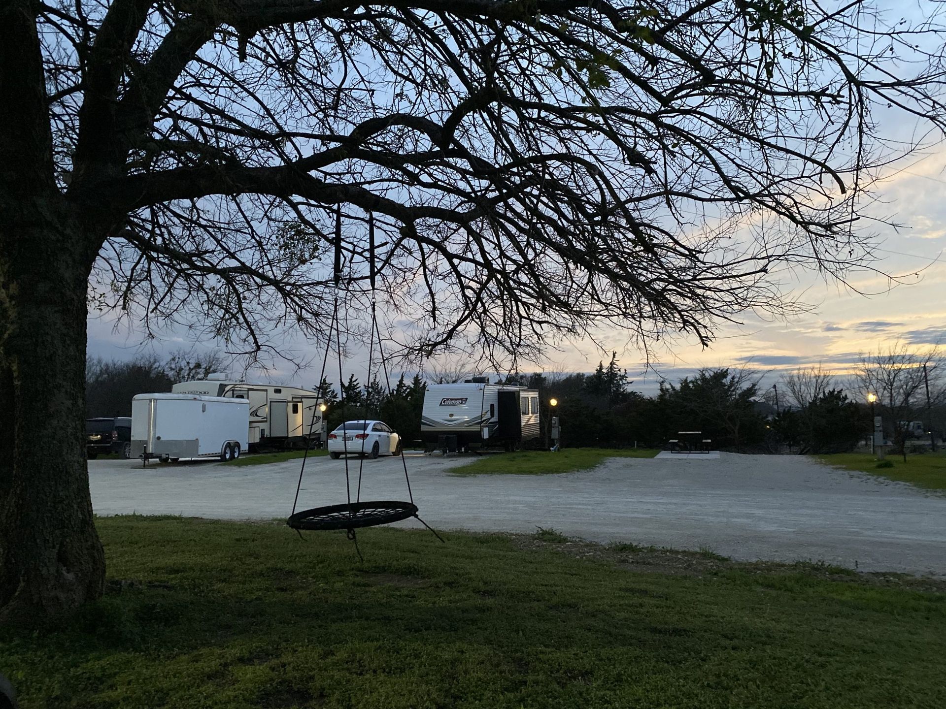 A tire swing hangs from a tree overlooking a parking area with trailers under a dusk sky.