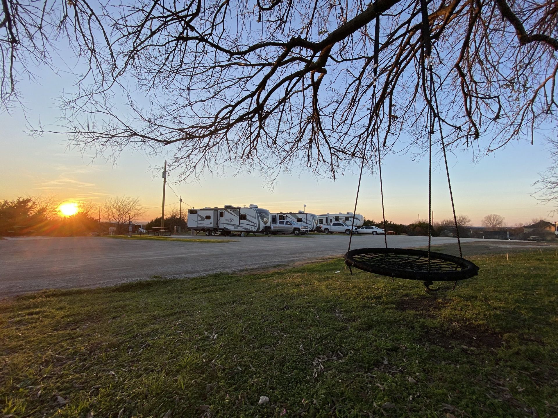Sunset over a campground with RVs, a tree swing in the foreground, and bare tree branches.