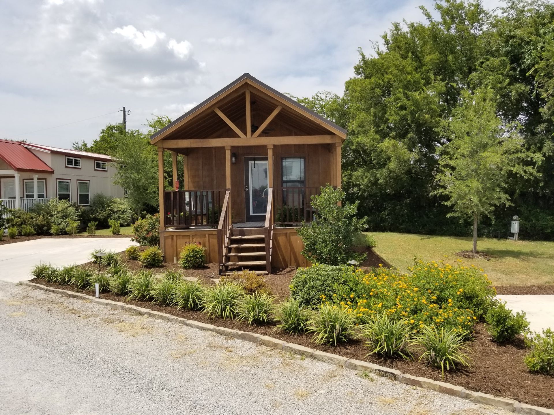 Small wooden cabin with porch, surrounded by landscaping, under a sunny sky.