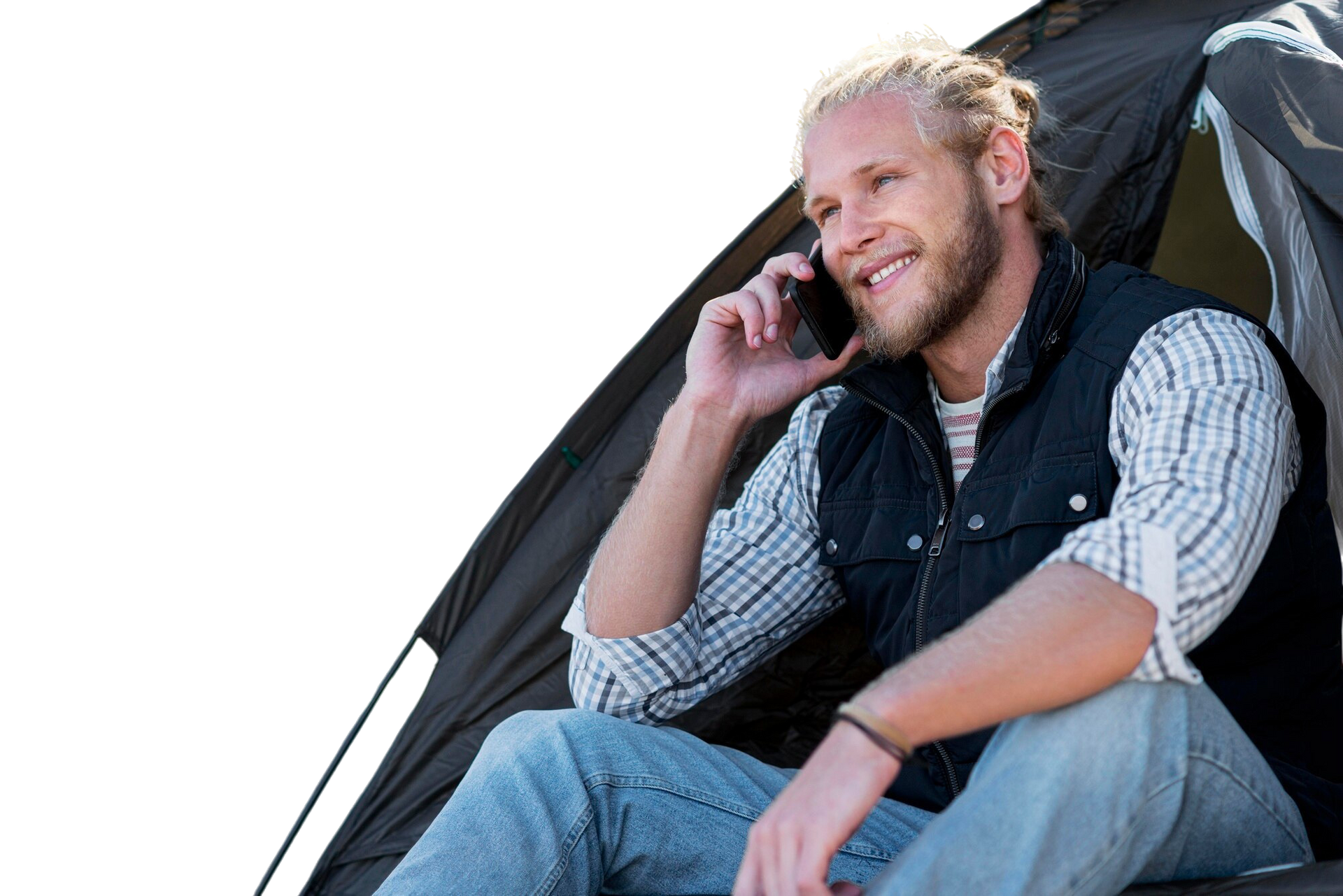 Man in tent smiles while on phone. He wears a vest, button-up shirt, and jeans.