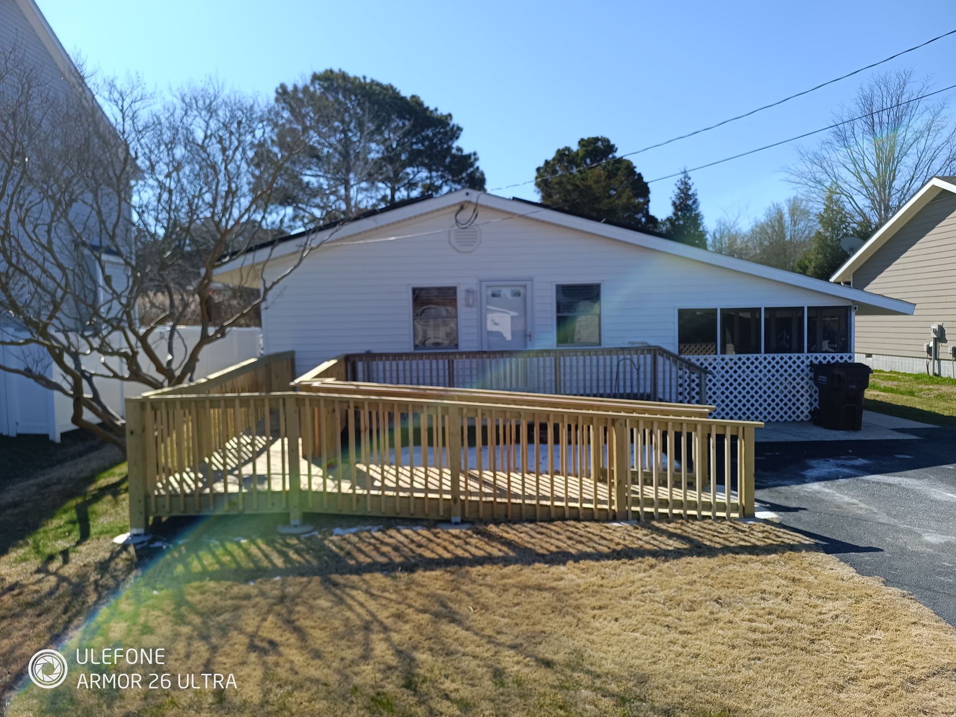 Wooden ramp leading to a white building with a deck. Sunny day.