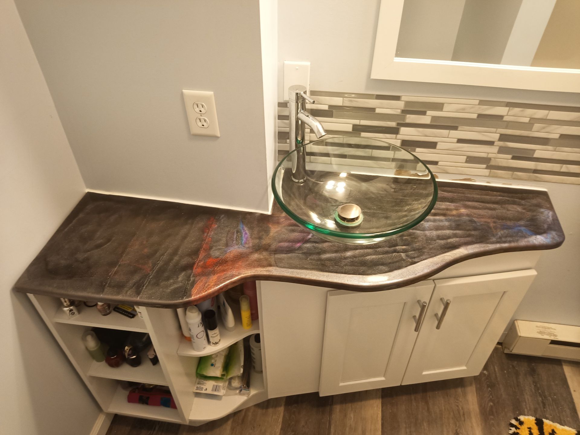 Bathroom vanity with glass sink, white cabinets, and dark countertop. Open shelves on left, tiled backsplash, and mirror.