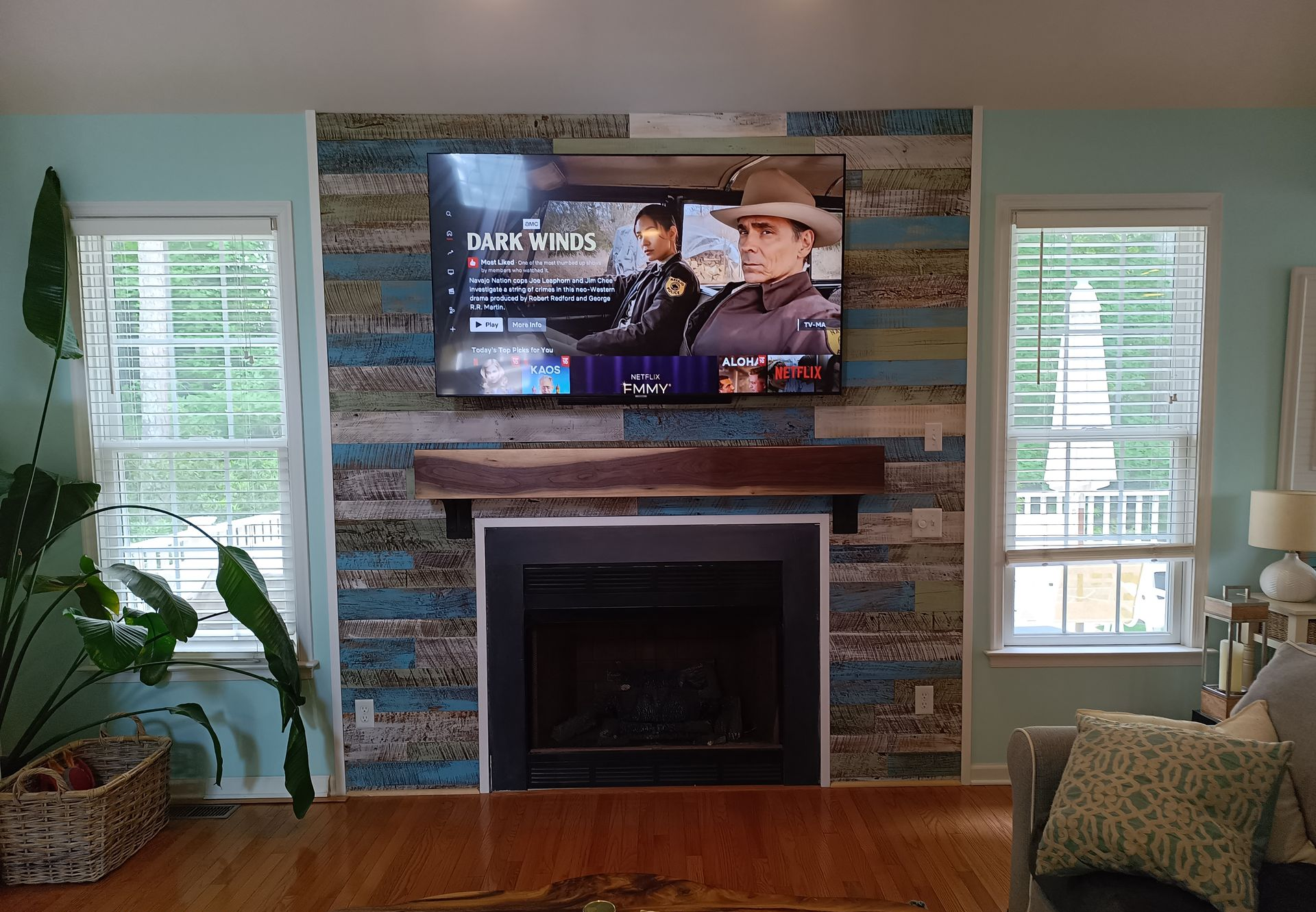 Living room with TV above fireplace. Turquoise and wood paneling on the wall. Windows on each side.