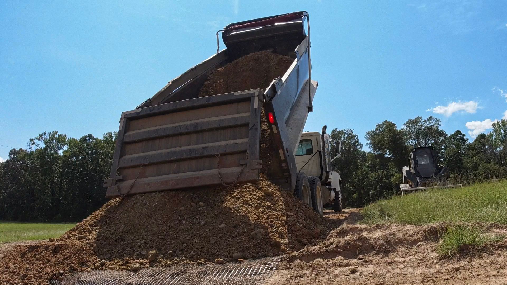 Yellow front loader filling a truck with gravel under a blue sky at a construction site.