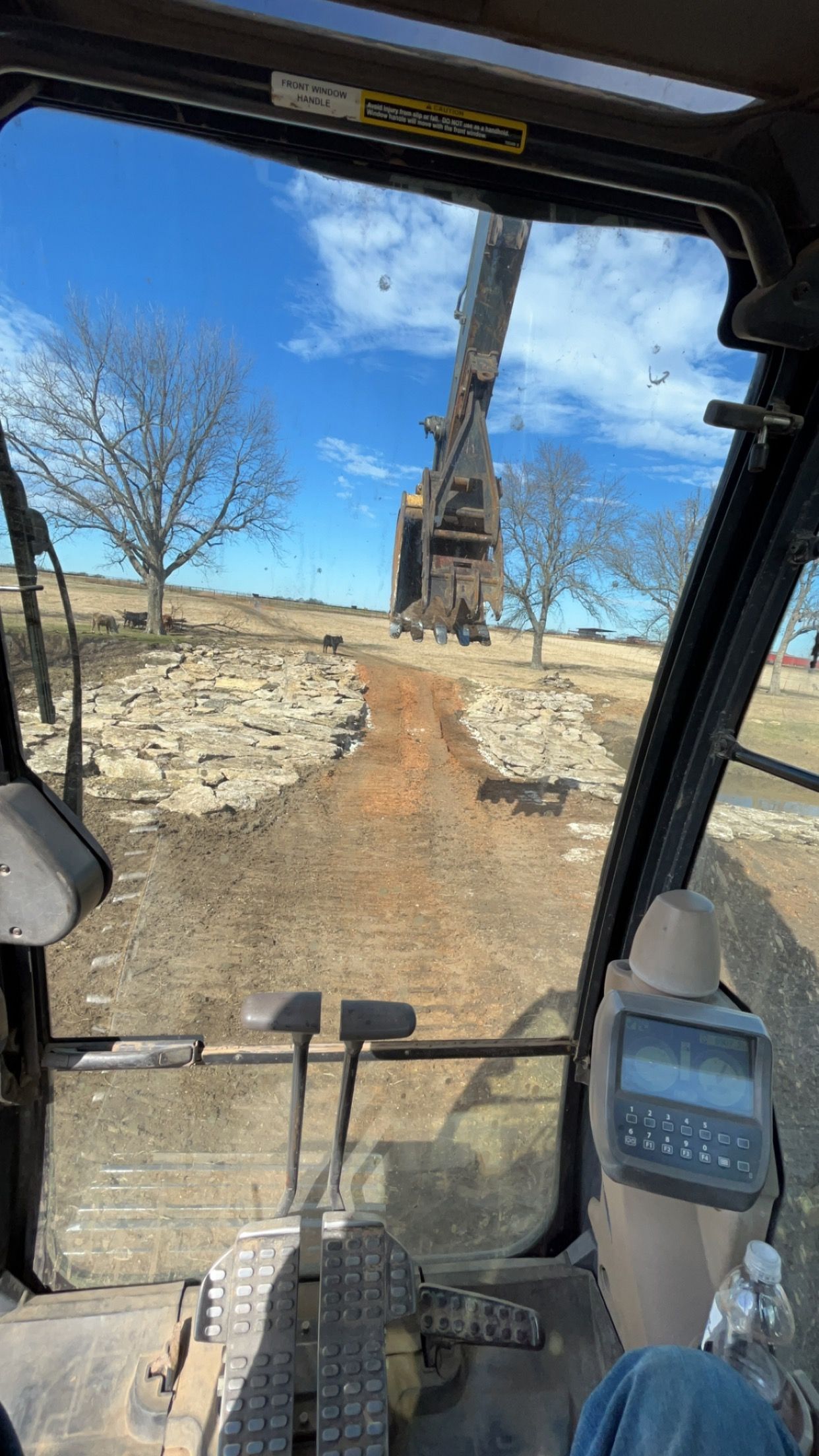 View from an excavator cab, looking towards a crane on a construction site under a blue sky.