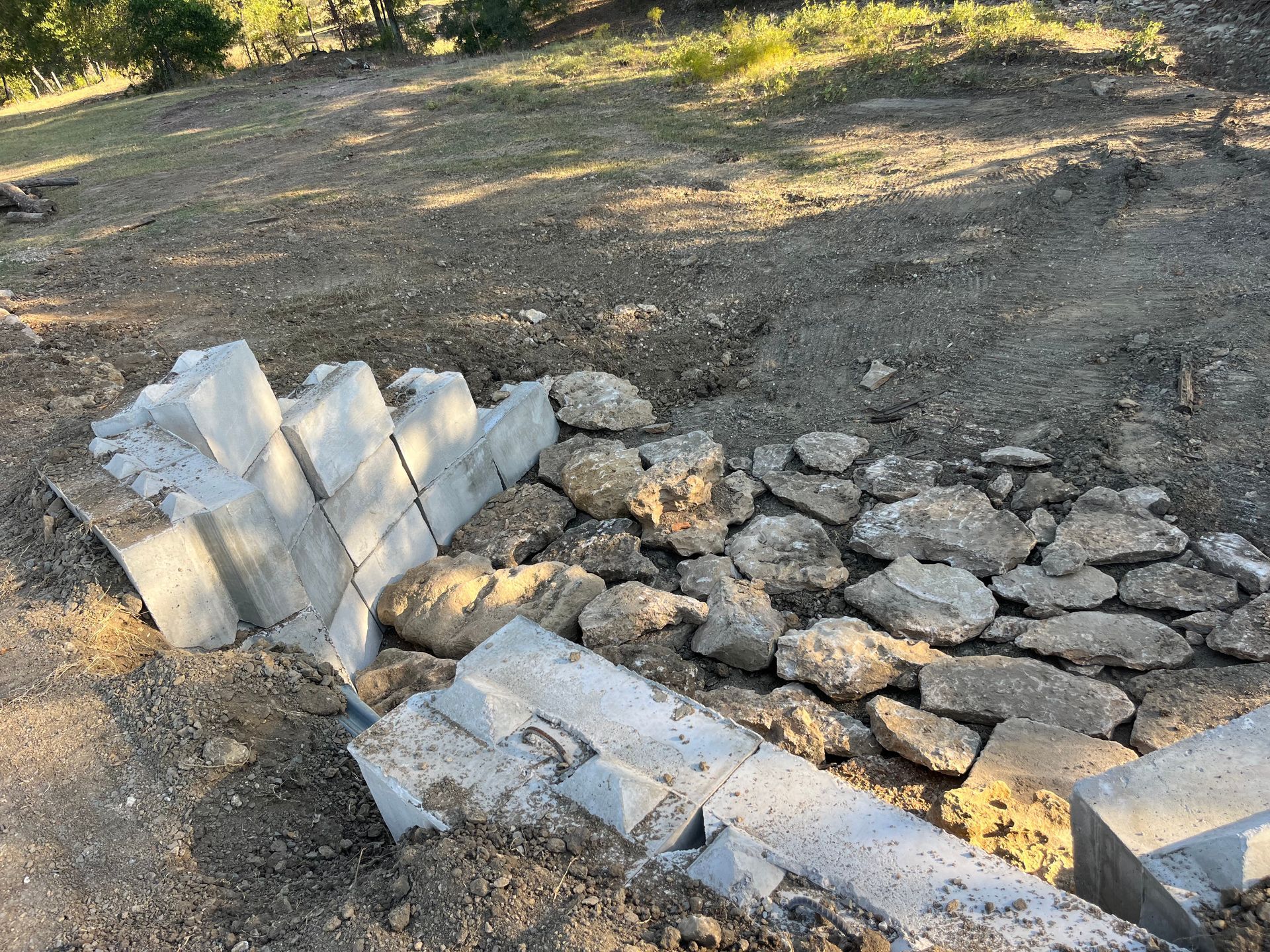 Concrete blocks and rocks arranged on dirt, possibly forming a retaining wall in an outdoor setting.