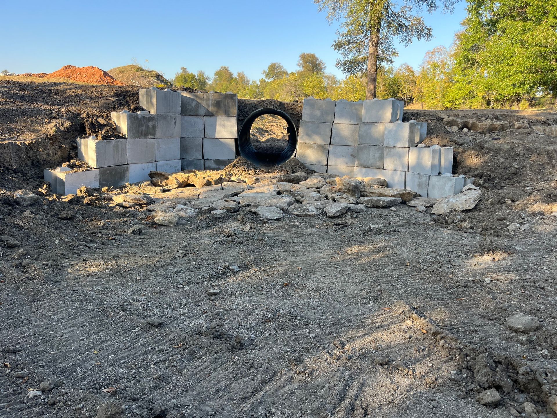 Concrete blocks forming a bridge around a culvert pipe; dirt and construction in the background.