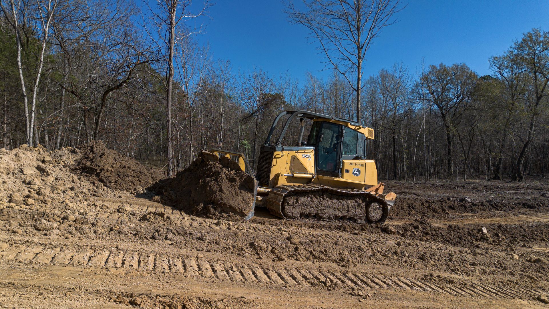 Yellow excavator on gravel pile in a forest, ready to dig.