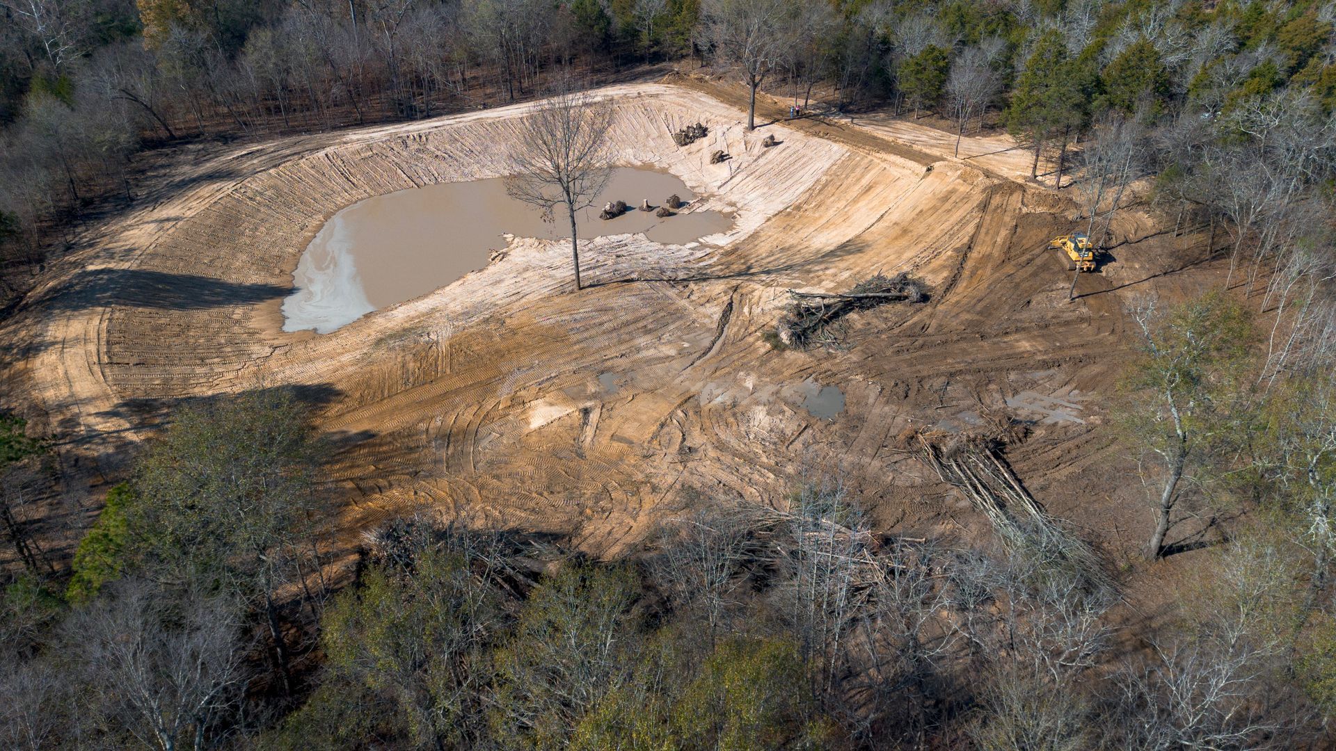 Green landscape with a pond, mountain view, cloudy sky.