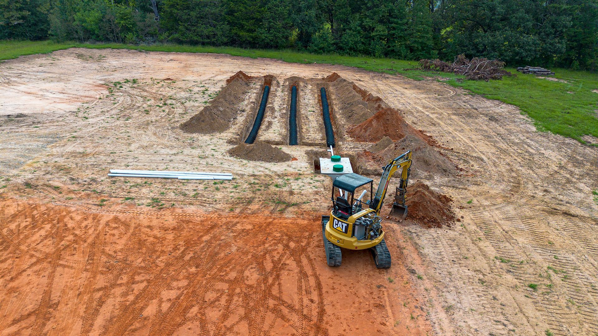An excavator bucket dumping dirt into a hole, revealing a dark cylindrical tank.