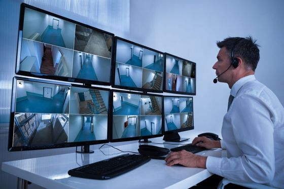 rear view of a male operator wearing headphone looking at multiple camera footage on computer