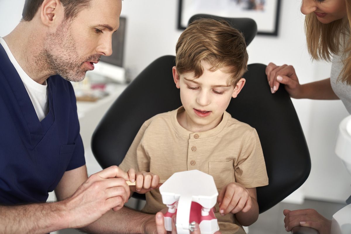 A young boy is sitting in a dental chair looking at a model of his teeth.