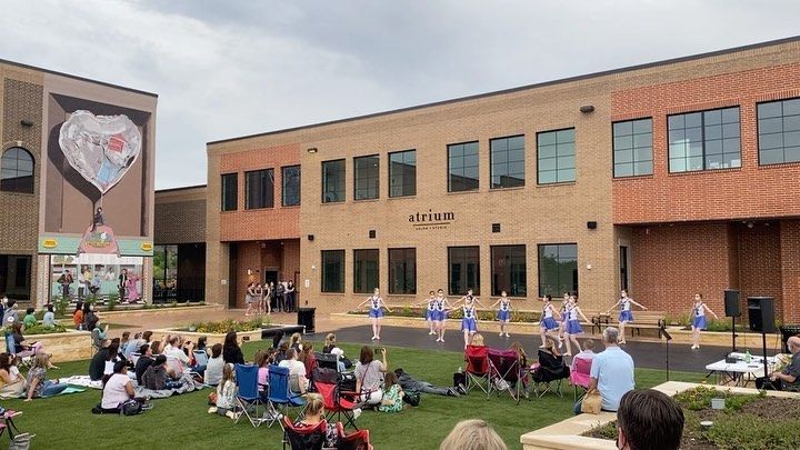 A group of people are sitting on the grass in front of a large brick building.