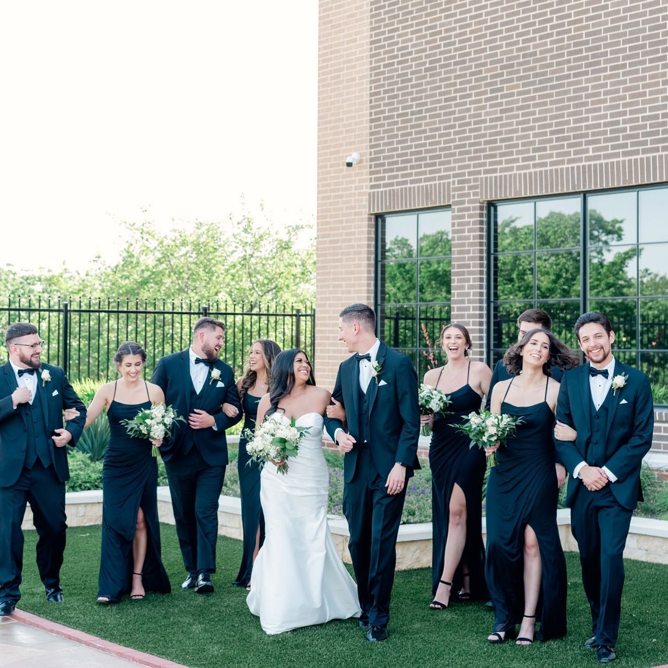 A bride and groom are walking with their wedding party in front of a brick building.