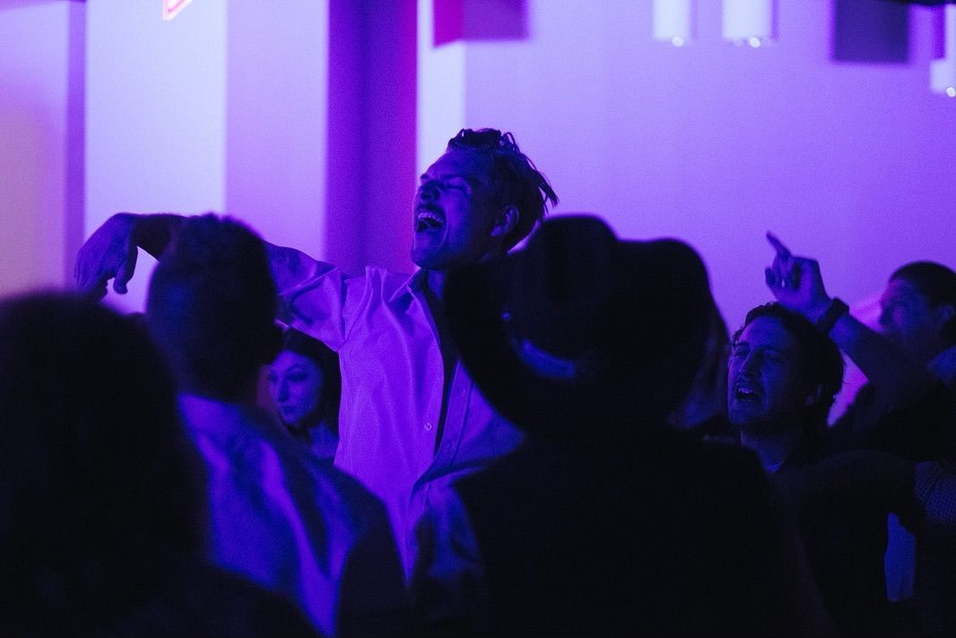 A group of people are dancing in a dark room with purple lights.