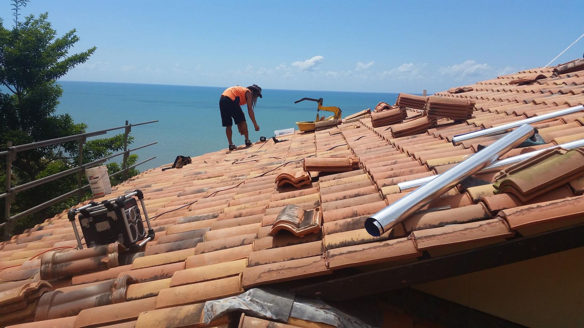 A Person Repairs a Tiled Roof with An Ocean View — High Performance Roof Tiling P/L in Kewarra Beach, QLD