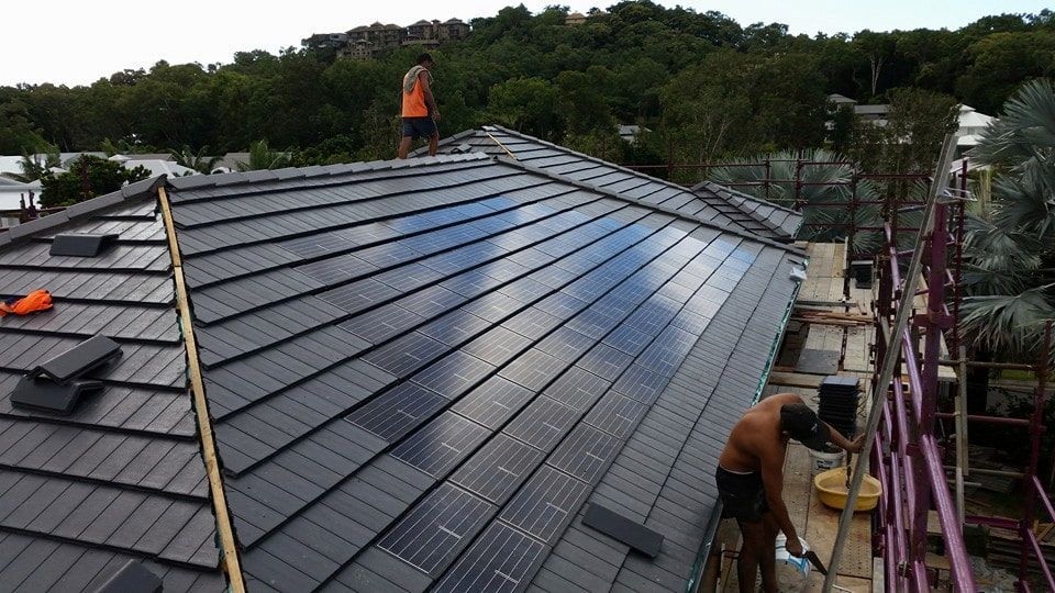 A Man is Working on the Roof of a House With Solar Panels — High Performance Roof Tiling P/L in Mareeba, QLD