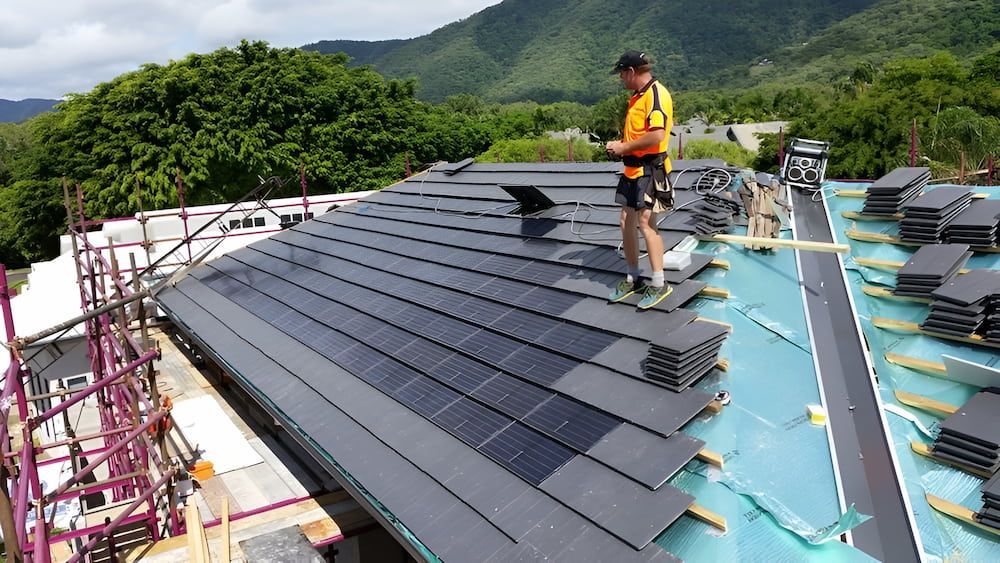 A Man is Standing on Top of a Roof With Solar Panels — High Performance Roof Tiling P/L in Kewarra Beach, QLD