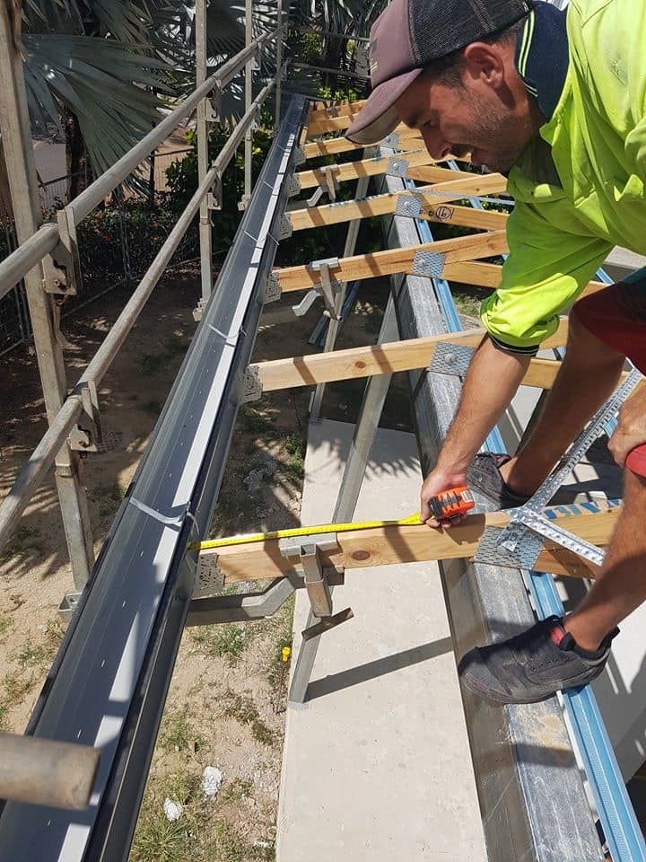 A Man is Measuring a Gutter With a Tape Measure — High Performance Roof Tiling P/L in Kewarra Beach, QLD