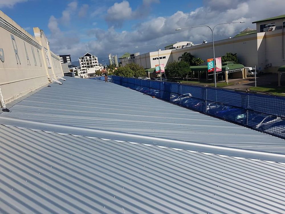 View of A Corrugated Metal Roof with A Blue Safety Fence, Buildings, and A Sunny Sky — High Performance Roof Tiling P/L in Kewarra Beach, QLD