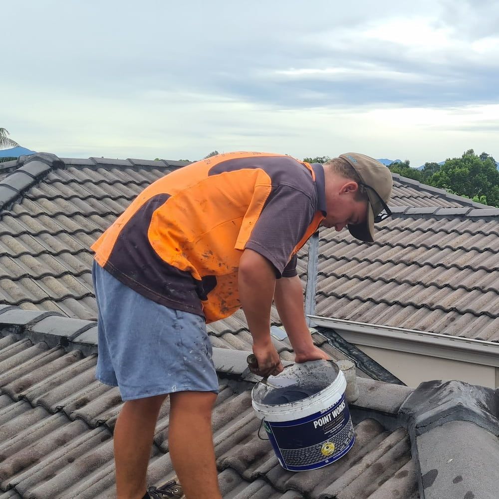 A Man is Working on a Roof With a Bucket of Paint — High Performance Roof Tiling P/L in Kewarra Beach, QLD