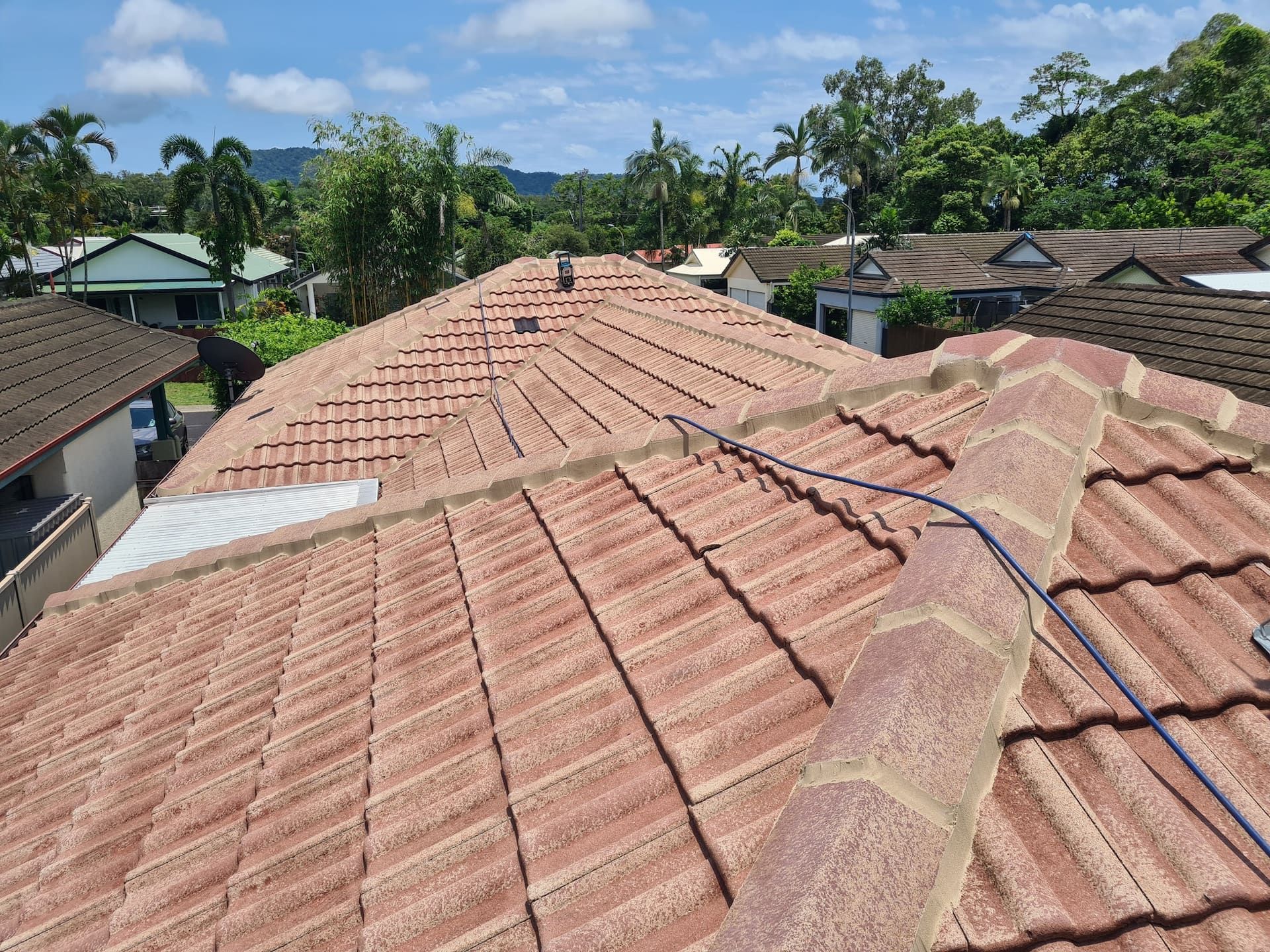 Red Tiled Roof with A View of Houses and Green Trees Under a Blue Sky — High Performance Roof Tiling P/L in Kewarra Beach, QLD