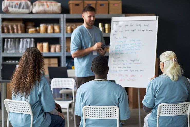 A man giving a presentation to a seated group of people at a community center; a whiteboard is visible.
