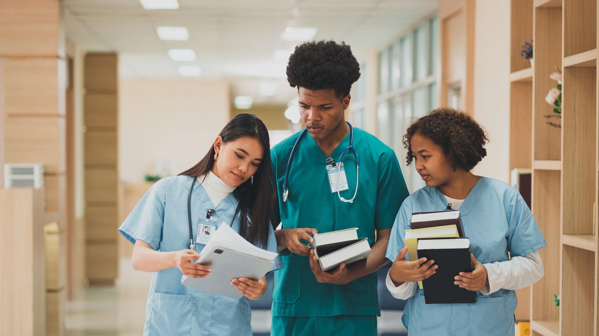 Three medical professionals in scrubs reviewing documents in a hospital hallway.