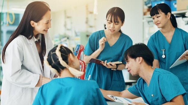 Medical team in scrubs and lab coat discussing patient chart, using a model in a lab.